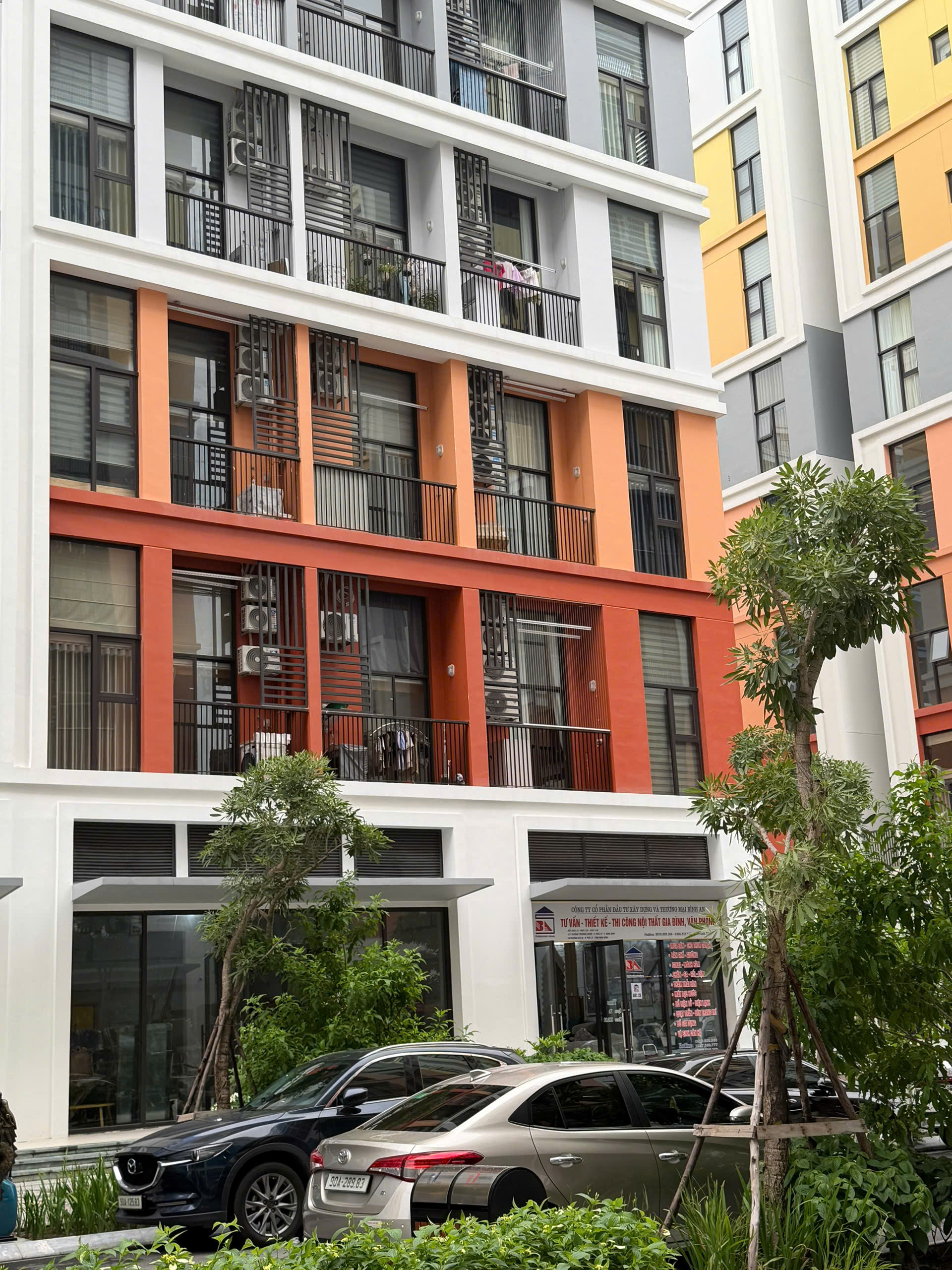 Mặt tiền chung cư hiện đại nhiều màu với ban công, cây xanh và ô tô đỗ phía trước